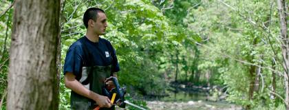 A person wearing hip waders stands outside, holding a measuring tool.